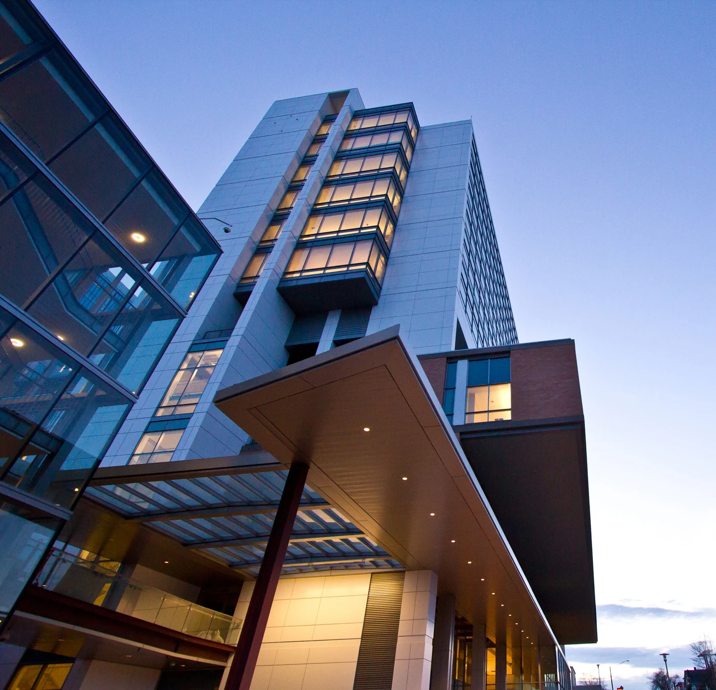 Low-angle view of a modern glass-and-concrete office building with illuminated windows against a blue dusk sky.