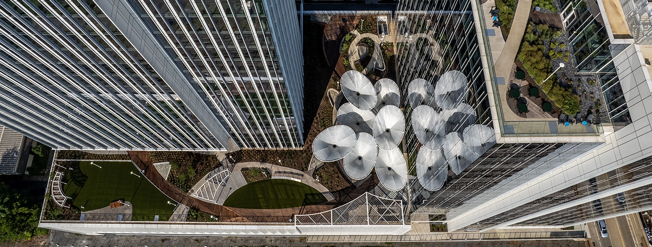 Aerial view of glass office towers with a rooftop terrace featuring overlapping circular metal sun shades and green spaces.