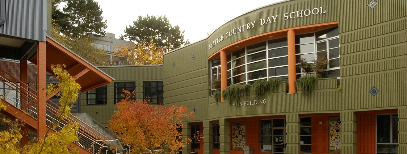 Facade of Seattle Country Day School main building with green brick walls and orange accents, autumn trees in foreground.