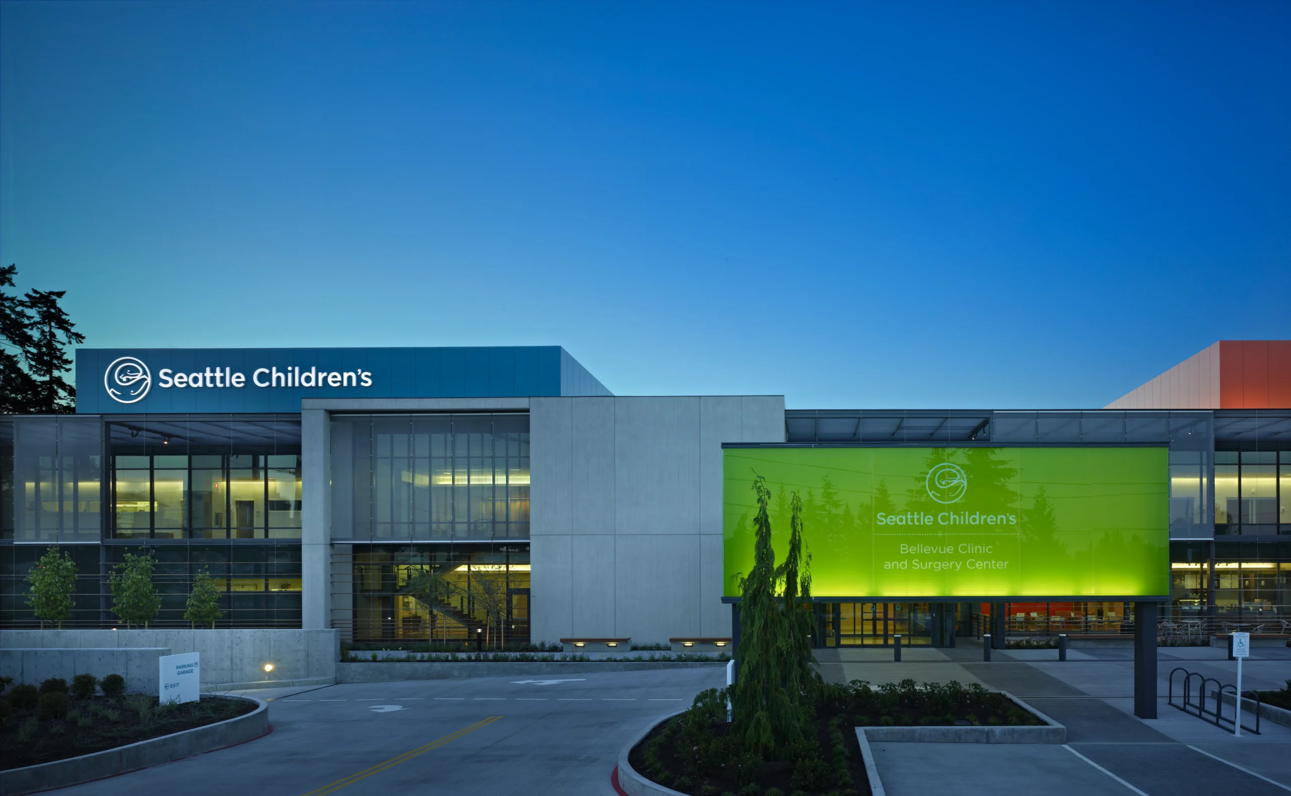 Exterior view of Seattle Children's clinic building with a blue sign and a bright green banner on the façade mentioning Bellevue Clinic and Surgery Center
